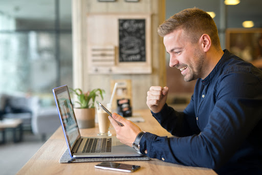 Happy freelancer with tablet and laptop computer in coffee shop.