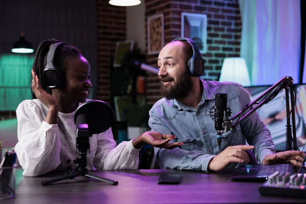 Cheerful man and woman using podcast equipment to livestream chat, recording discussion on camera to create social media content. Online vloggers live broadcasting talk show video.
