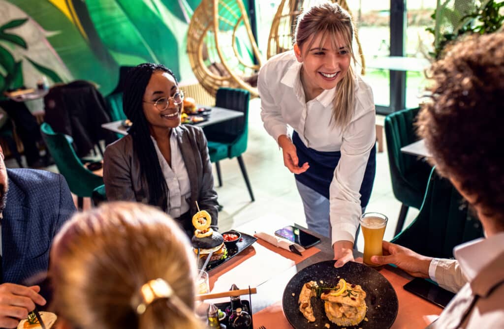 Smiling waitress serving meal to group of business people in restaurant.